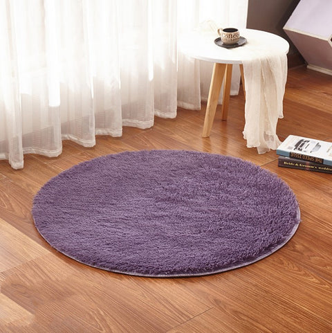 Round purple rug on a wooden floor with a small table and white curtains in the background.