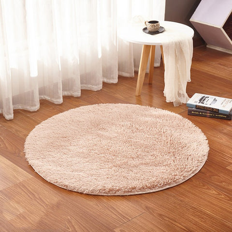 Round beige rug on a wooden floor with a small table and white curtains in the background.