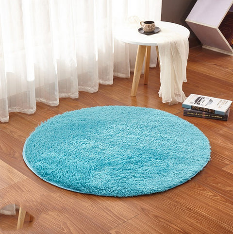 Round turquoise rug on a wooden floor with a small table and books in the background.
