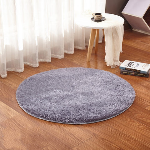Round gray rug on a wooden floor with a small table and books in the background.
