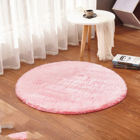 Round pink rug on a wooden floor with a small table and books in the background.
