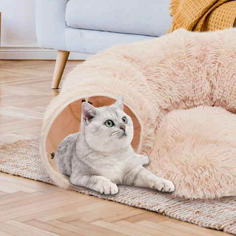Cat lying inside a fluffy cat house on a wooden floor with a light-colored couch in the background.
