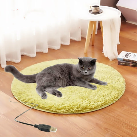 Cat lying on a round yellow heating pad with a USB cable, in a home setting.